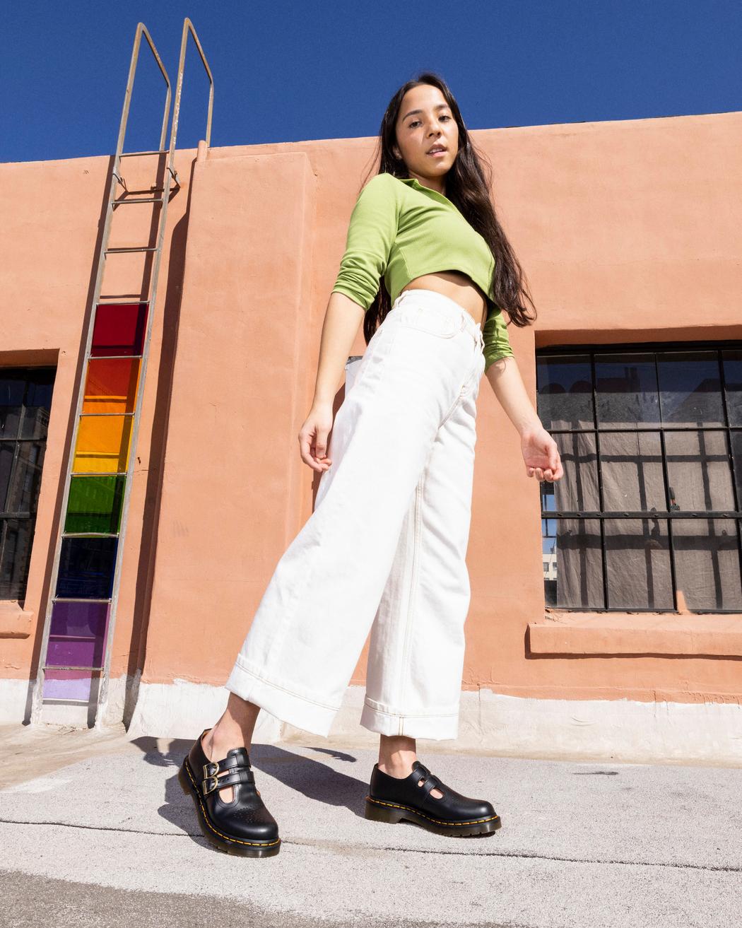 A model wearing a black leather Dr. Martens mary jane shoe with brass buckles.
