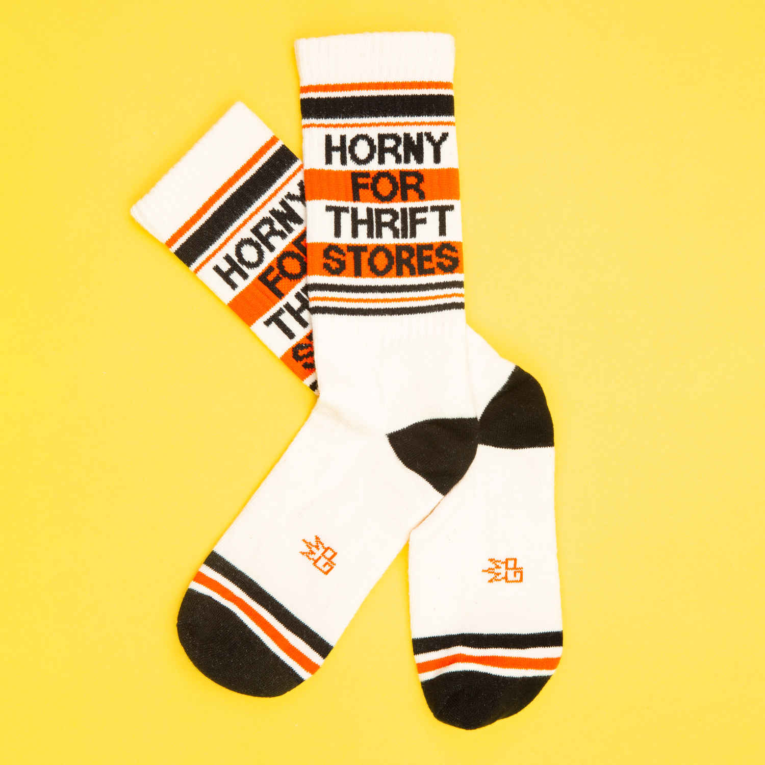 A pair of off-white and red crew socks that read "horny for thrift stores" with the Gumball Poodle logo on the arch.