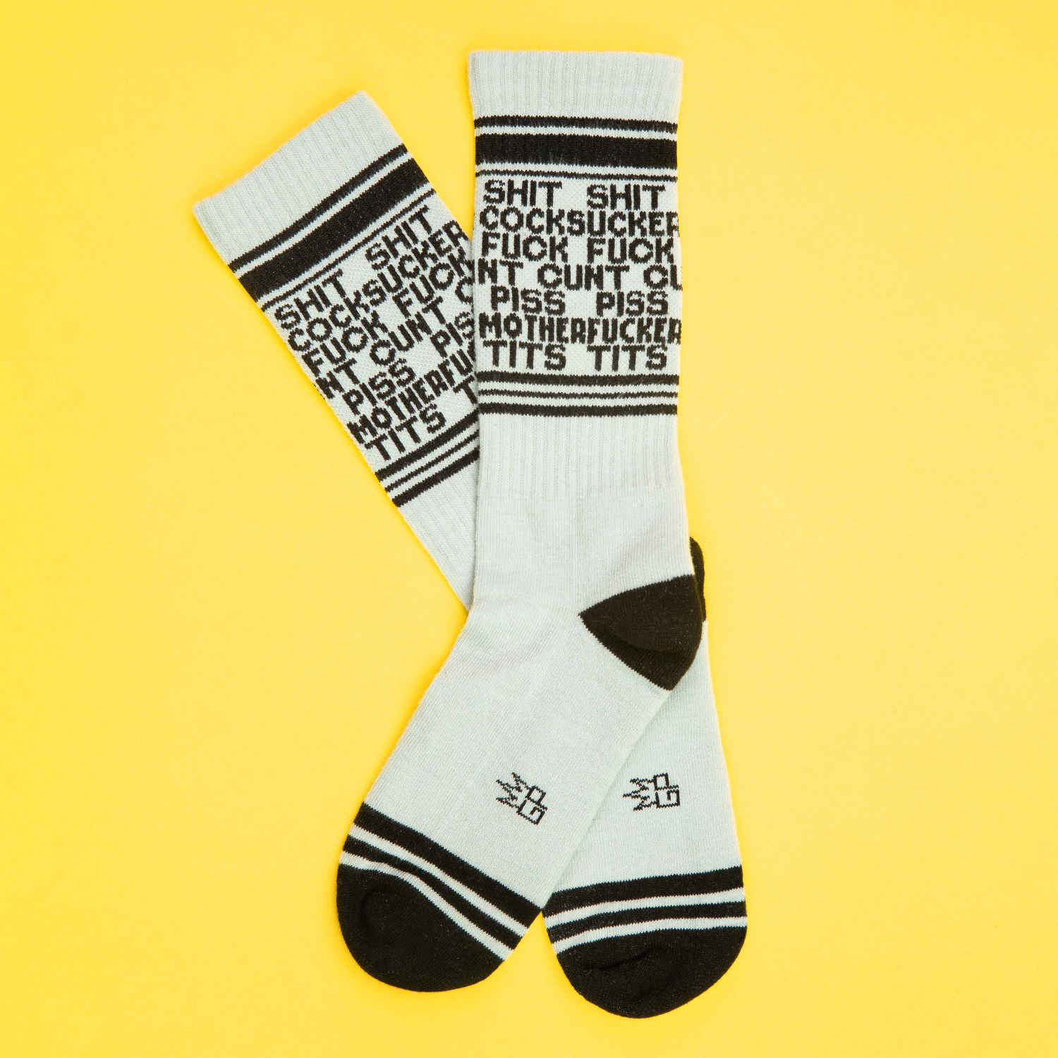 A pair of grey and black crew socks that read "shit cocksucker fuck cunt piss motherfucker tits" repeatedly with the Gumball Poodle logo along the arch.